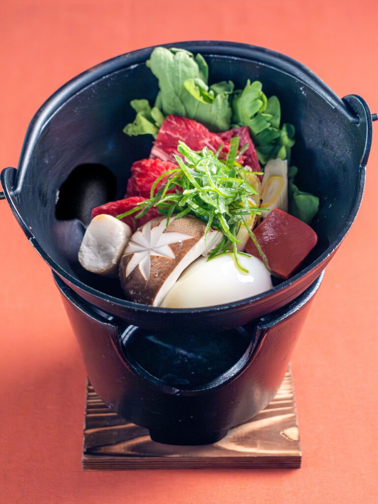 Steaming Japanese soup with beef, vegetables, and mushrooms served in black bowl at a Japanese soba restaurant