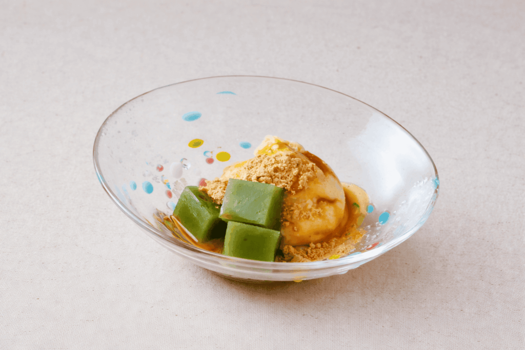 Japanese dessert with vanilla ice cream, matcha jelly cubes, and kinako in a glass bowl