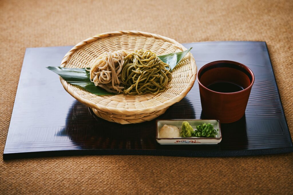 Cold soba noodles served on a bamboo tray with dipping sauce and condiments