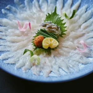 Delicately arranged fugu sashimi in a chrysanthemum pattern with garnishes, served at a luxury Japanese ryokan with private onsen on Awaji Island.
