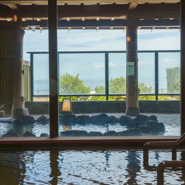 Indoor hot spring bath with natural stone design and large windows overlooking greenery and ocean at a luxury ryokan on Awaji Island.