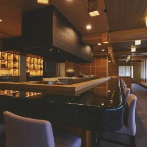 Elegant sushi bar with granite counter, wooden accents, and curated Japanese ceramics at a luxury Japanese ryokan with private onsen on Awaji Island.