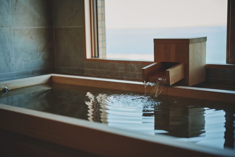 Cypress wooden soaking tub with flowing water and ocean view in a deluxe Japanese‑style room at a luxury ryokan on Awaji Island.