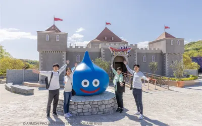 Visitors posing with Dragon Quest slime statue at Nijigen no Mori on Awaji Island in front of themed castle attraction