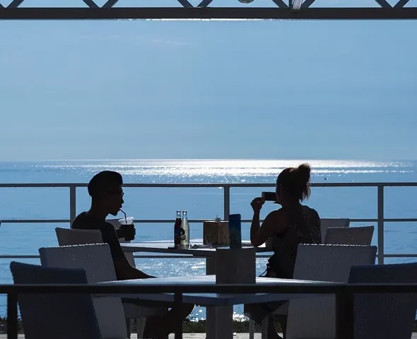 A silhouette of people dining on a terrace at Miele restaurant, overlooking the sparkling blue ocean.